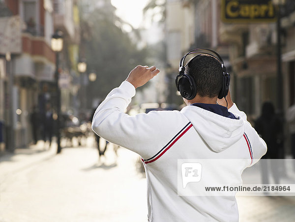 Young man standing in street wearing headphones  rear view