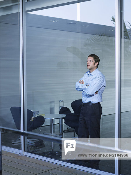 Young businessman standing at window in office  arms crossed