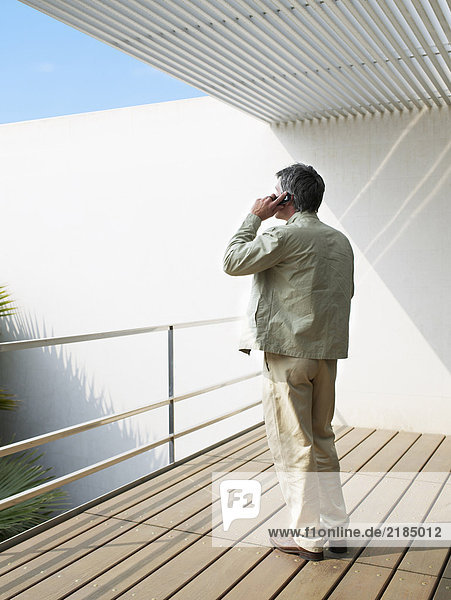 Mann auf Balkon stehend mit Handy  Rückansicht