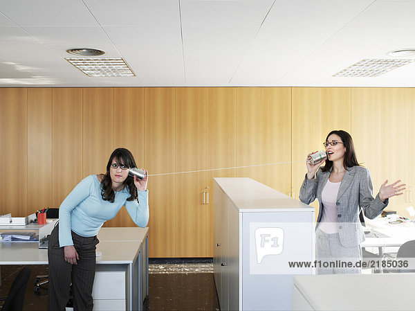 Two businesswomen using tin cans to communicate in office