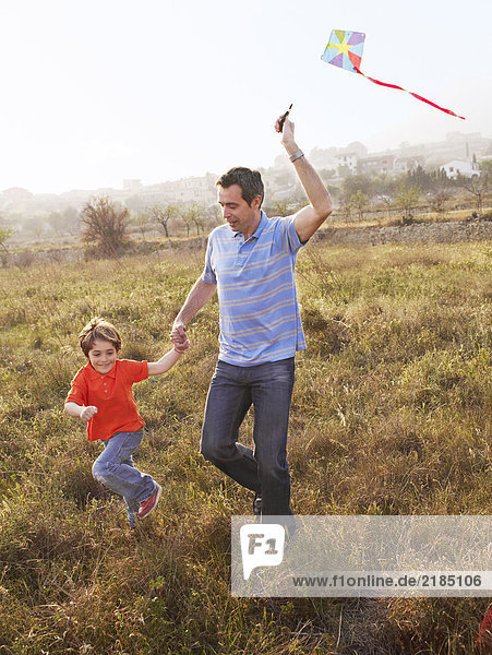 Vater und Sohn (4-6) laufen im Feld mit Drachen  lächelnd