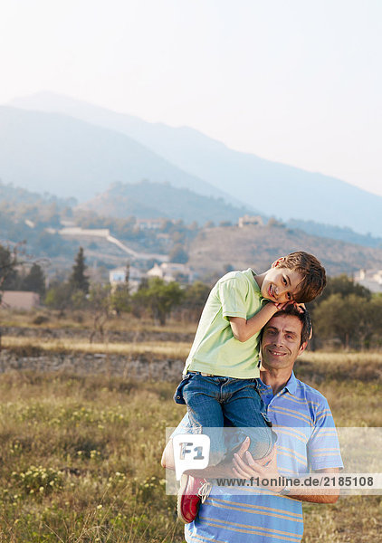 Father carrying son (6-8) in field  smiling  portrait