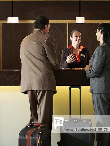 Hotelrezeptionistin im Gespräch mit Geschäftsmann und Frau  lächelnd