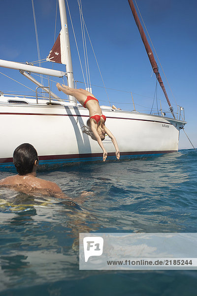 Junge Frau taucht von der Yacht ins Meer  Mann im Vordergrund