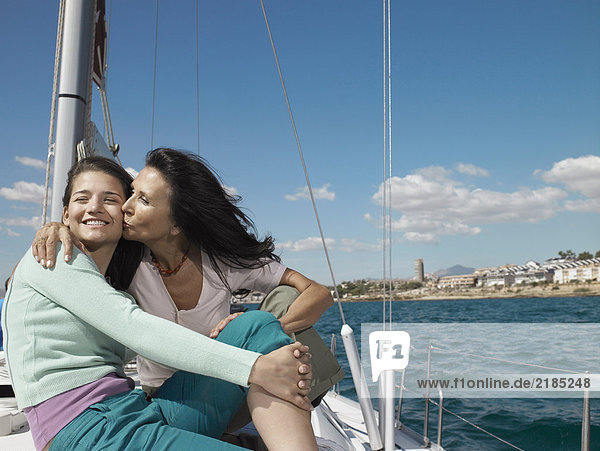 Mature mother kissing daughter on yacht  smiling