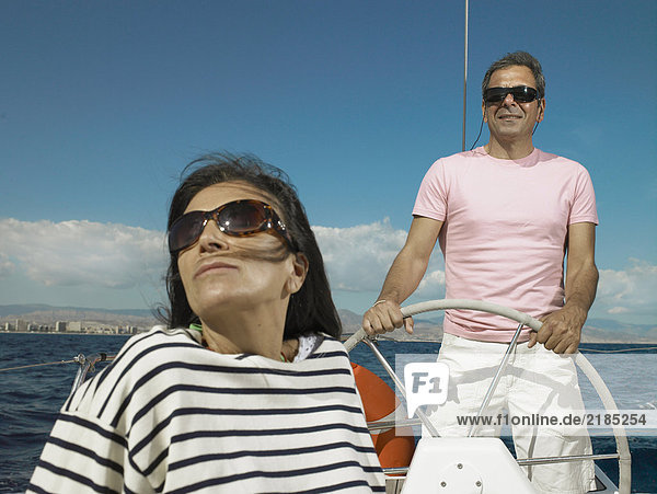 Mature couple wearing sunglasses sailing yacht