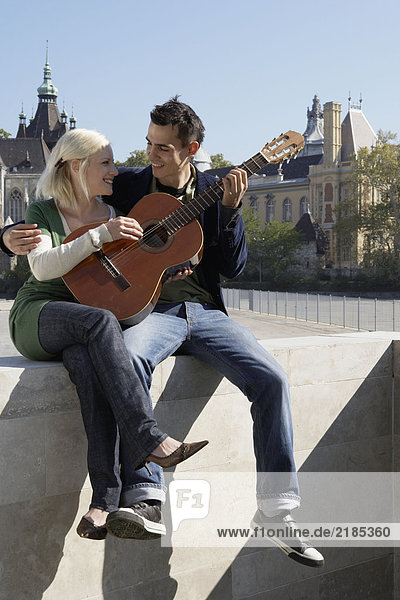 Ein Paar spielt Gitarre im Freien und lächelt.