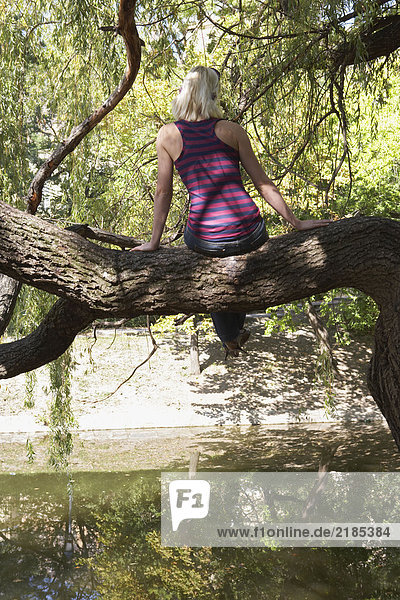 Frau sitzt auf einem Baum am See.