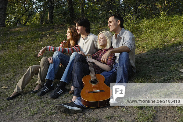 Vier Freunde sitzen mit einer Gitarre im Freien und lächeln.