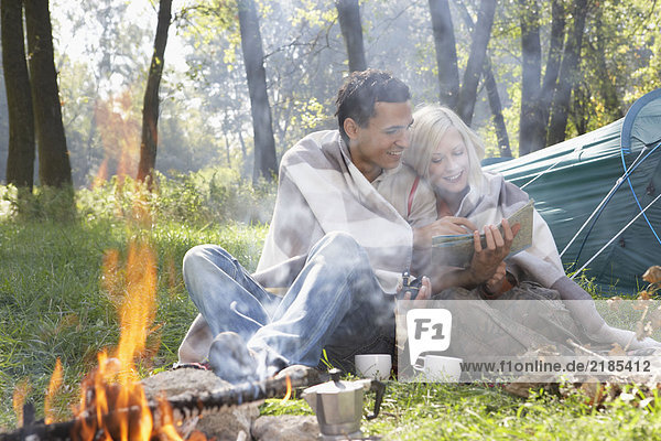 Ein Paar sitzt auf dem Campingplatz und schaut auf die Karte am Feuer lächelnd.
