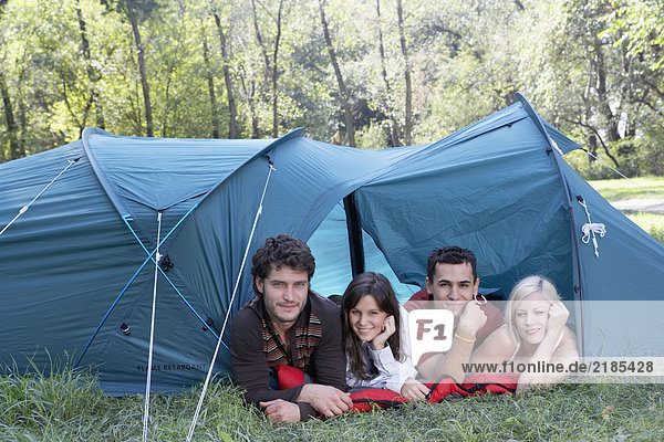 Vier Menschen liegen lächelnd in einem Zelt auf dem Campingplatz.