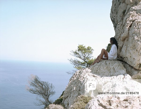Frau sitzt auf großen Felsen am Meer und entspannt sich.