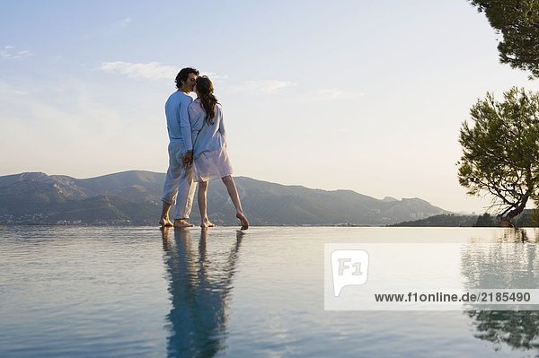 Couple kissing and holding hands by infinity pool.