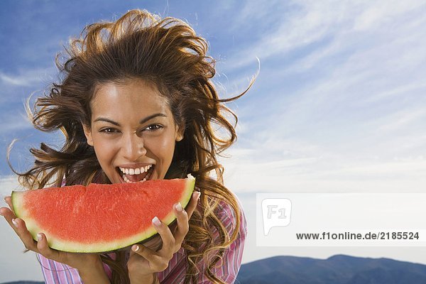 Frau lacht und isst Wassermelone im Freien.