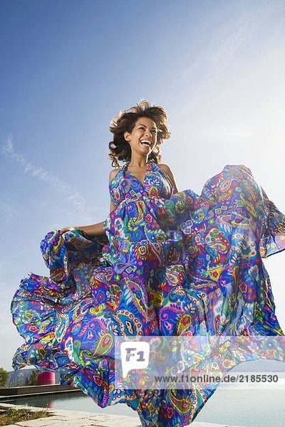 Dynamische Schönheitsfrau  die im Freien in einem bunten langen Sommerkleid lacht.