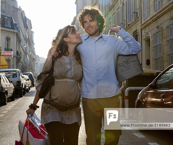 Schwangere junge Frau und junger Mann  die auf der Straße gehen  lächelnd