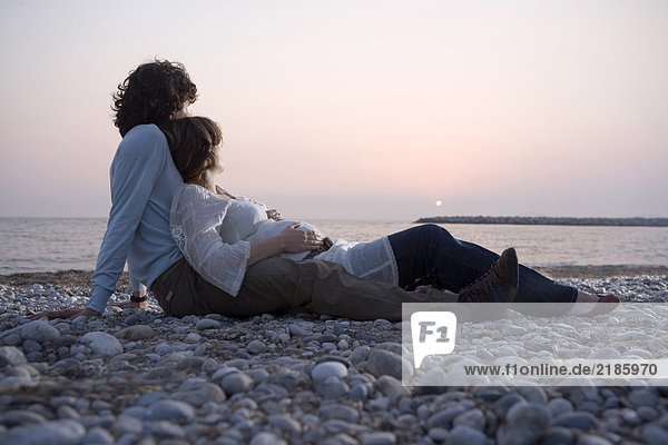 Young couple lying on beach  woman pregnant  sunset