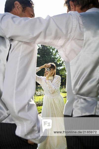 Junge Braut fotografiert Bräutigam und Vater in Gärten