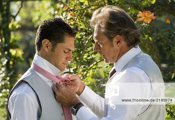 Erwachsener Vater hilft Bräutigam mit Krawatte im Garten