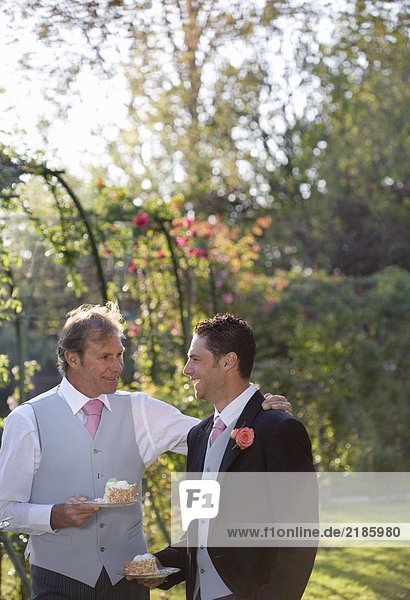 Reife Vater und Bräutigam halten Teller von Hochzeitstorte im Garten