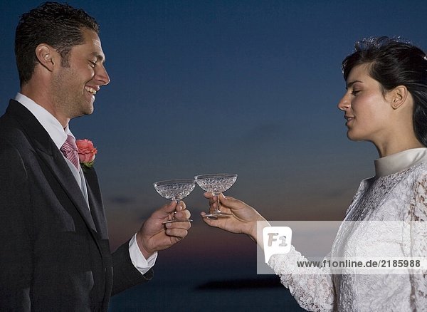 Braut und Bräutigam toasten sich gegenseitig mit Champagner  lächeln  Sonnenuntergang