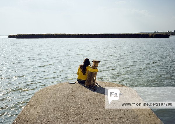 Mädchen sitzend mit Hund am See Rückansicht.