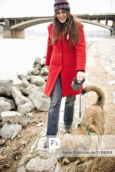 Junge Frau mit Hund an der Leine am Fluss lächelnd