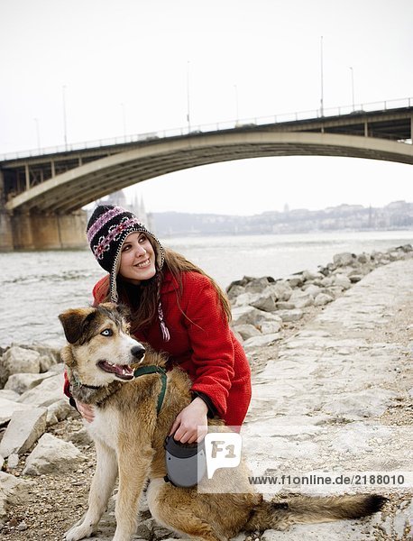 Junge Frau kniend mit Hund am Flussufer  lächelnd
