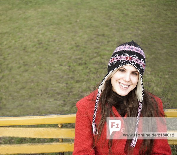 Junge Frau mit Hut auf Bank sitzend  lächelnd  Portrait