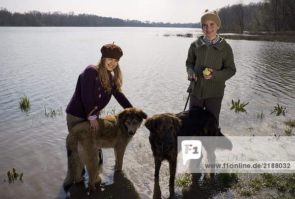 Brother (12-14) and sister (11-13) standing in river with two dogs  smiling