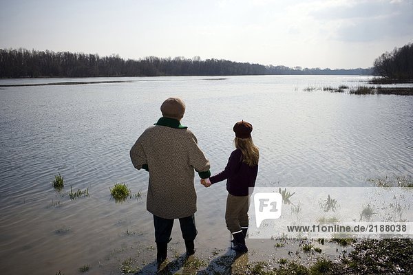 Grandmother and granddaughter (10-12) standing in river  rear view