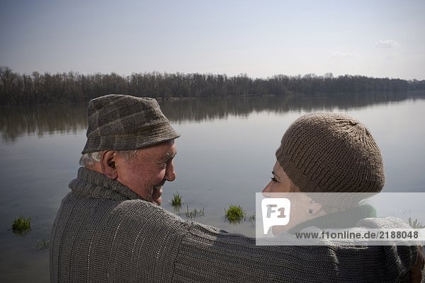 Senior couple by river  man holding arm around woman  rear view