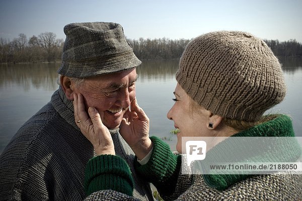 Senior couple by river  woman touching man's face  smiling  close-up