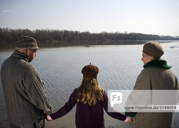 Grandparents holding hands with granddaughter (10-12) by river
