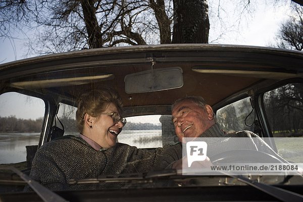 Älteres Ehepaar sitzt im Auto und lächelt sich an