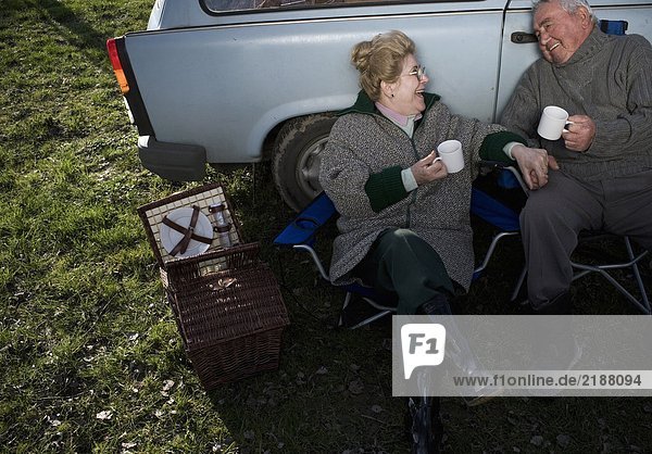 Senior couple having picnic by car  holding cups  smiling