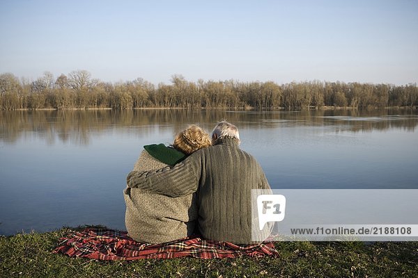 Senior couple sitting on rug by river  rear view
