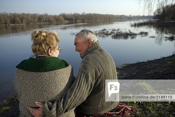 Senior couple sitting on rug by river  rear view  man smiling