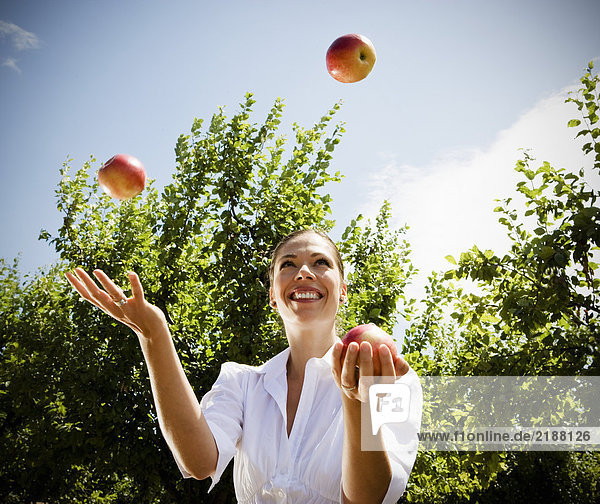 Frau jongliert mit Äpfeln im Obstgarten.