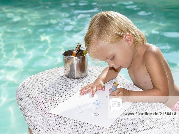 Ein kleiner Junge malt am Pool.