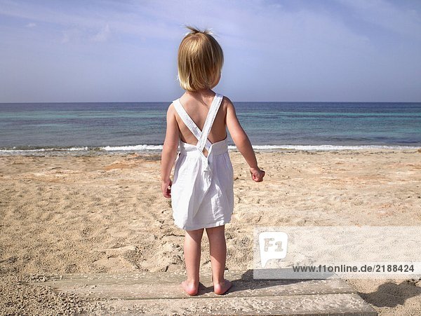 Kleiner Junge  der auf einem Holzweg am Strand steht.
