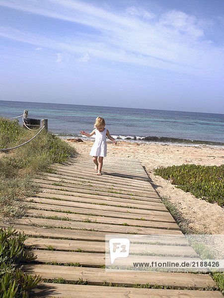 Young boy walking on a wooden path at the beach.