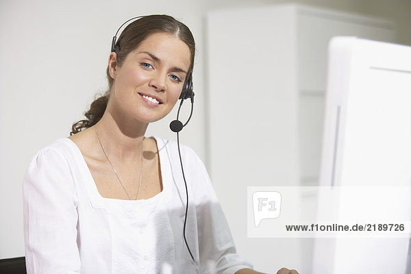 Smiling woman at computer desk using headset.