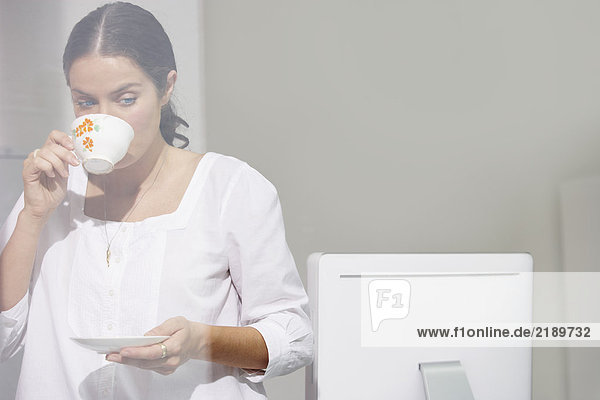 Frau trinkt Tee am Computertisch.