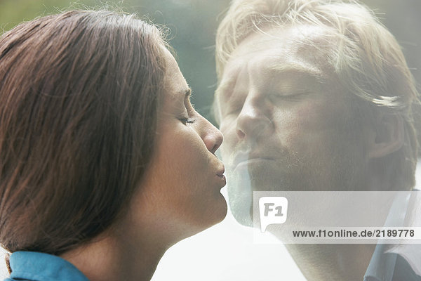 Ein junges Paar  das sich durch ein Glas Fenster küsst.
