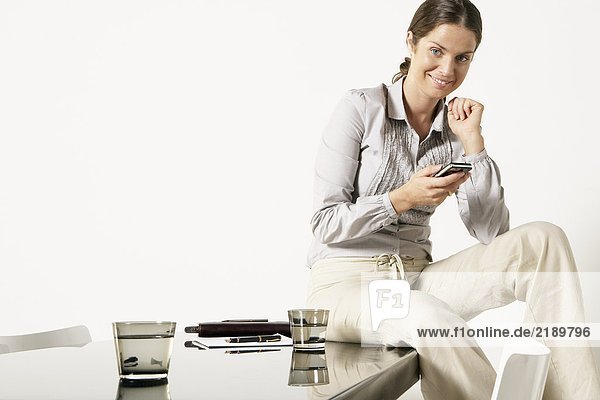 Junge Geschäftsfrau sitzt auf dem Schreibtisch und sendet eine SMS.