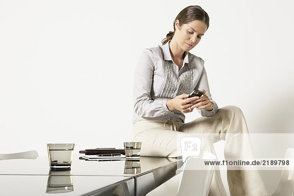 Junge Geschäftsfrau sitzt auf dem Schreibtisch und sendet eine SMS.