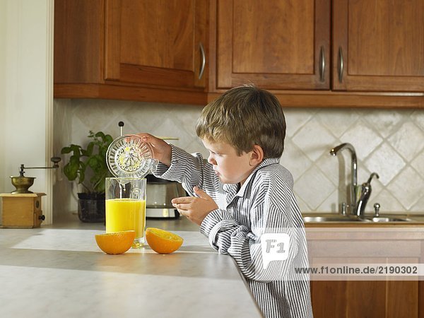 Ein kleiner Junge macht Orangensaft in der Küche.