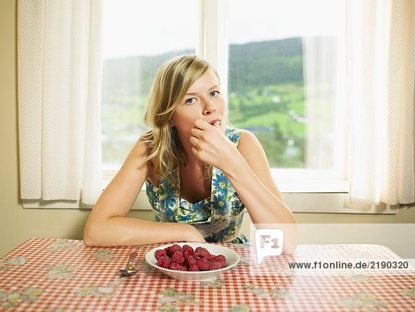 Woman eating bowl of raspberries at table.