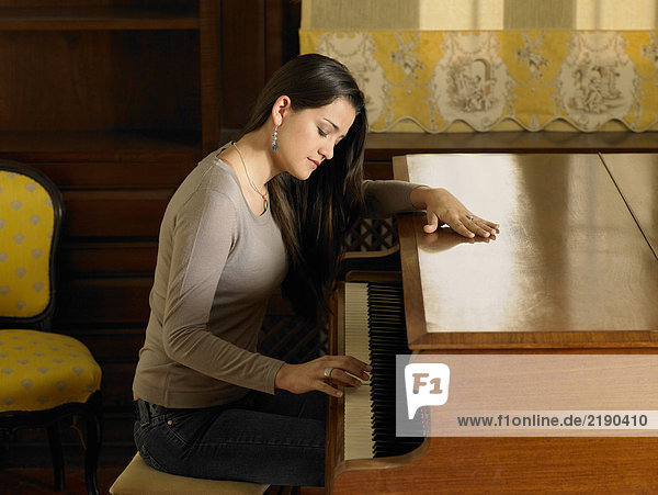Junge Frau beim Klavierspielen mit einer Hand  Seitenansicht